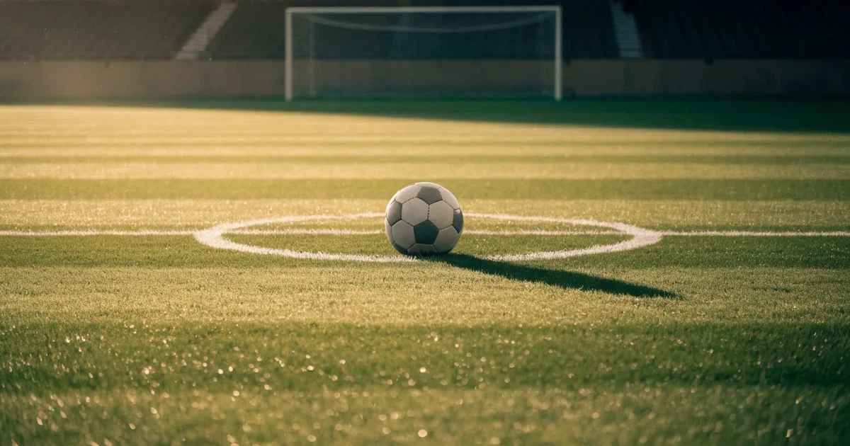 Uma bola de futebol no ponto central de um relvado, à luz da manhã